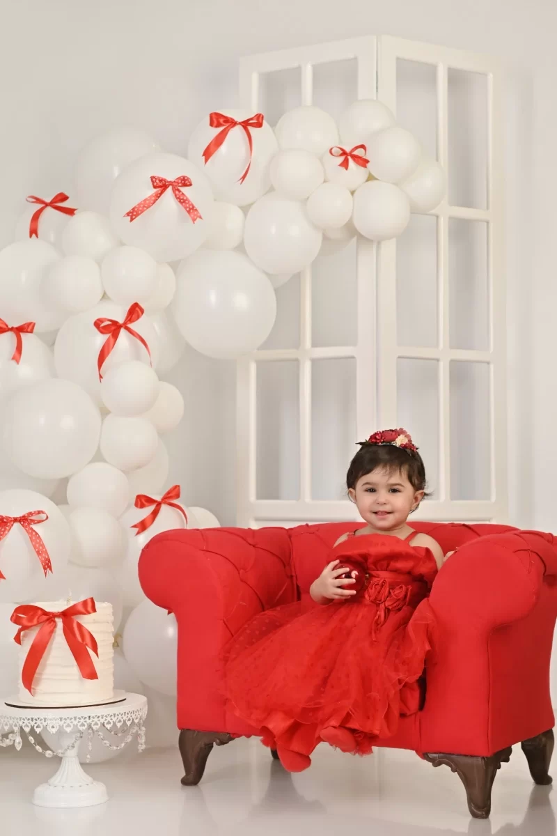 عکس تولد با تم قرمز و دکور بادکنک و کیک و صندلی به همراه پایپون های قرمز